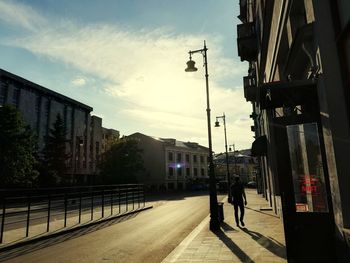 Silhouette people walking on street amidst buildings against sky