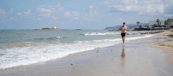 Front view of man jogging at beach against sky