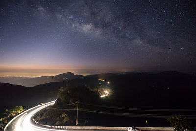 Road amidst illuminated mountains against sky at night