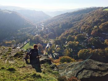 Rear view of mature woman sitting on mountain against sky during sunny day