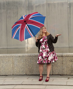 Full length portrait of woman with british flag umbrella on sidewalk
