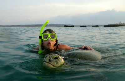 Young woman by turtle in sea against sky