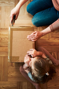 Woman unpacking a cardboard box parcel in room at home. little girl waiting for opening a box