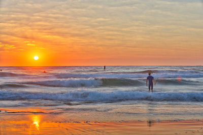 Rear view of man standing at beach against sky during sunset