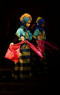 People in traditional clothing standing against black background