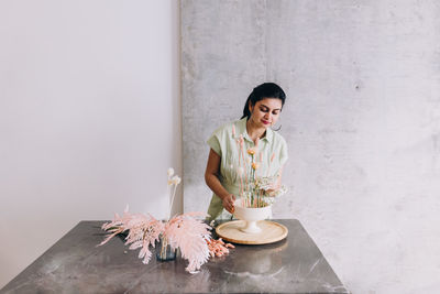 Portrait of young woman standing against a concrete wall, working with flowers 