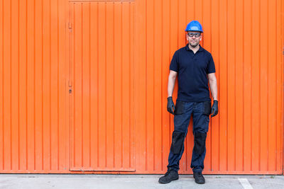 Full length portrait of man standing against orange wall