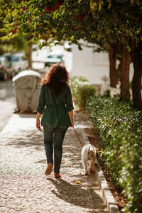 Rear view of woman with dog walking on footpath