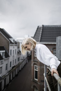 Side view of woman looking down while leaning on balcony railing