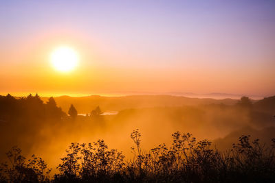 Scenic view of foggy landscape against sky during sunset