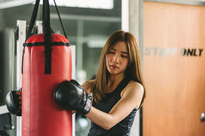 Confident young woman holding punching bag while standing in gym