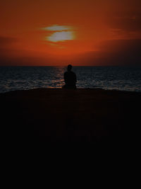 Silhouette of man looking at sea against sunset sky