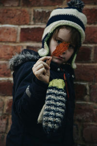 Boy holding autumn leaf against brick wall