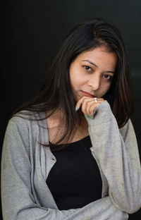 Portrait of beautiful young woman sitting against black background