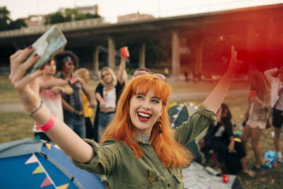 Happy young woman taking selfie with friends while camping during music festival