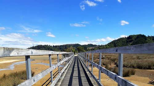 Footbridge over calm blue sea against sky
