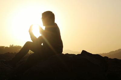 Man sitting on rock against clear sky