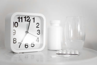 White alarm clock and pills with glass of water on table. it's time to take the medicine.