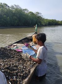 Side view of young man standing by boat in river