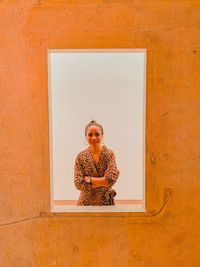 Portrait of a smiling young woman standing against wall