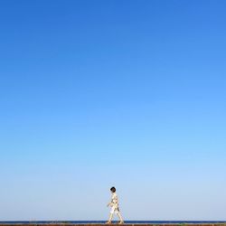 Side view of woman walking against clear blue sky
