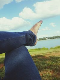 Low section of man sitting on grass against sky