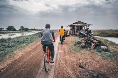 Rear view of man riding bicycle on road against sky