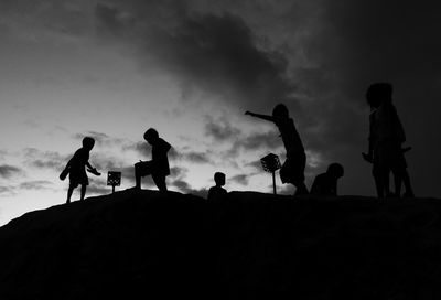 Silhouette of children playing against cloudy sky