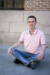 Portrait of young man sitting against wall