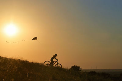 Silhouette people riding bicycle on field against sky during sunset