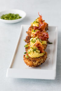 A row of deep fried gourmet deviled eggs garnished with chives and prosciutto.