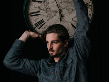 Portrait of young man standing against black background