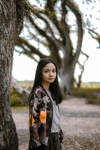 Portrait of young woman standing by tree trunk