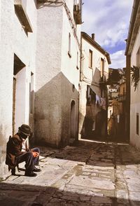 Full length of man sitting by building on alley