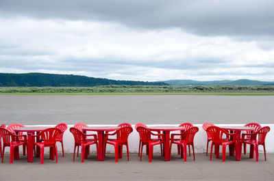 Cafe outdoors. red plastic tables and chairs by the river on a background of hills.