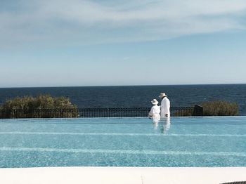 Couple standing by swimming pool against sky