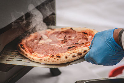 Hand with plastic glove cooking or baking hot pizza with tomato sauce, mozzarella and salami meat