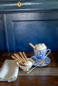 Gourmet hot chocolate and whip cream in a nautical china mug with cookies on a rustic table 