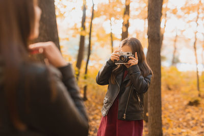 Woman holding camera while standing by tree during autumn