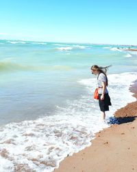 Side view of woman standing at beach against sky