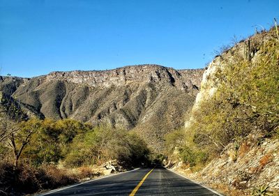 Road leading towards mountains against clear blue sky