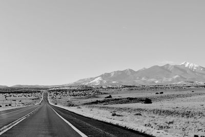 Road leading towards mountains against clear sky