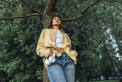 Woman with eyes closed relaxing in front of tree