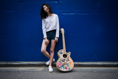 Portrait of a woman with guitar against blue wall