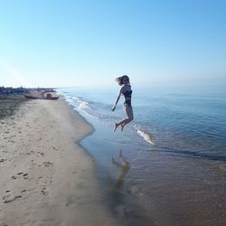 Full length of woman jumping at beach against clear sky