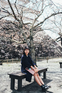 Portrait of young woman sitting on bench by cherry tree