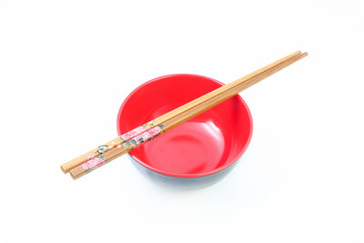 High angle view of chopsticks on red ceramic bowl against blue background