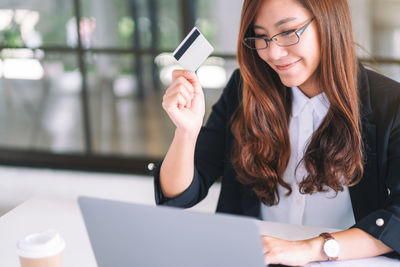 Mid adult woman using laptop while holding credit card over table