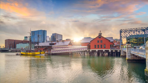 Buildings by river against sky during sunset