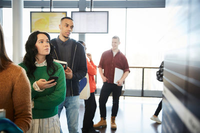 Male and female young bored students waiting in line at university